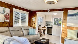 Een moderne woonkamer met een beige leren bank, een houten eettafel en een keuken met witte kastjes en een roestvrijstalen vaatwasser.