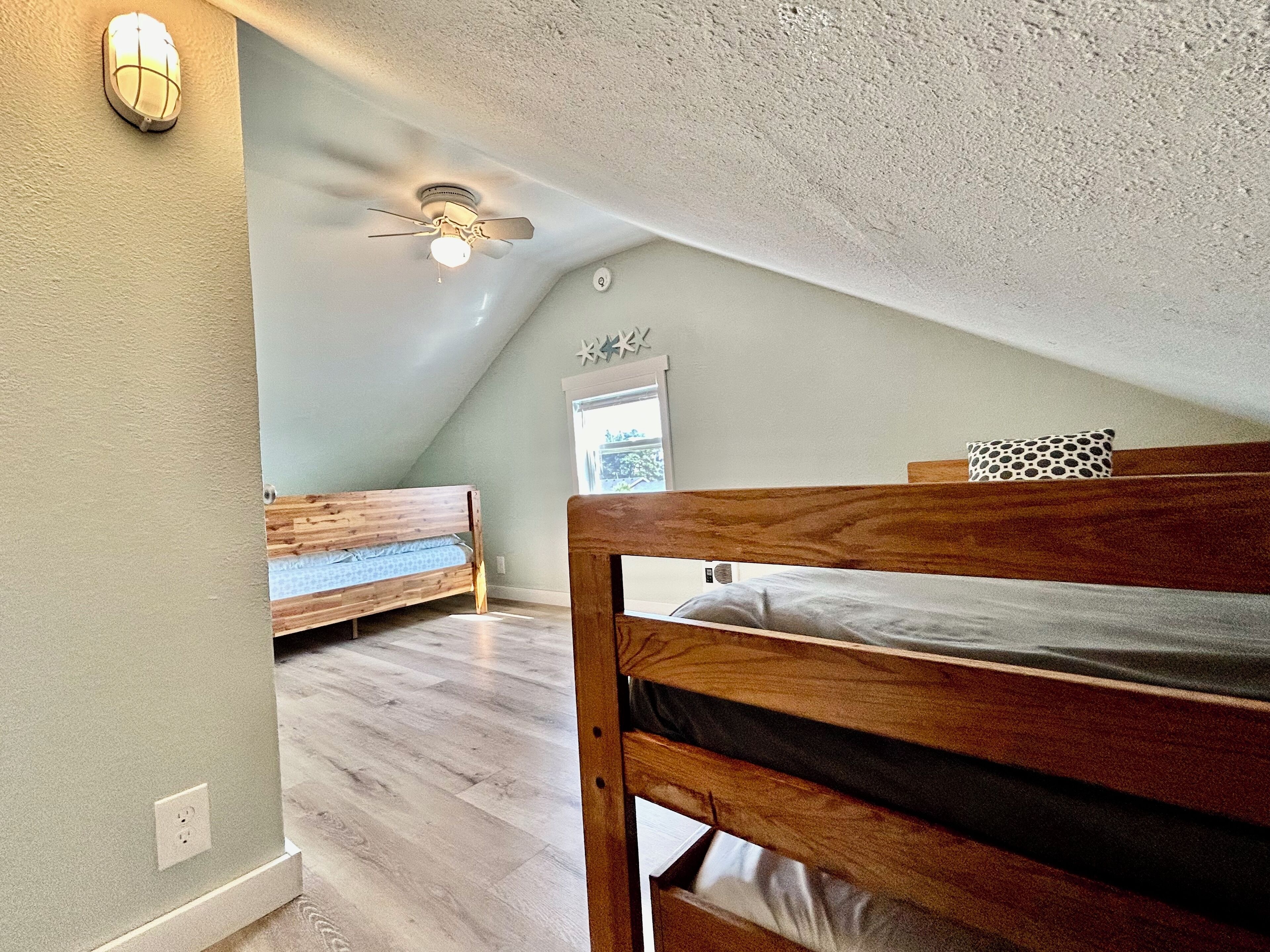 A bedroom with a sloped ceiling, a ceiling fan, and two wooden beds.
