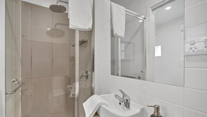 Une salle de bain moderne avec une douche à parois de verre, un lavabo blanc avec un miroir au-dessus, et une serviette accrochée au mur.
