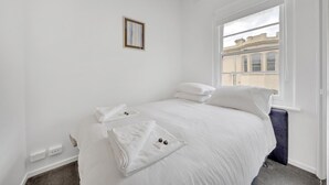 Un dormitorio minimalista con una cama grande, una ventana con vistas a edificios y un cuadro pequeño en la pared.