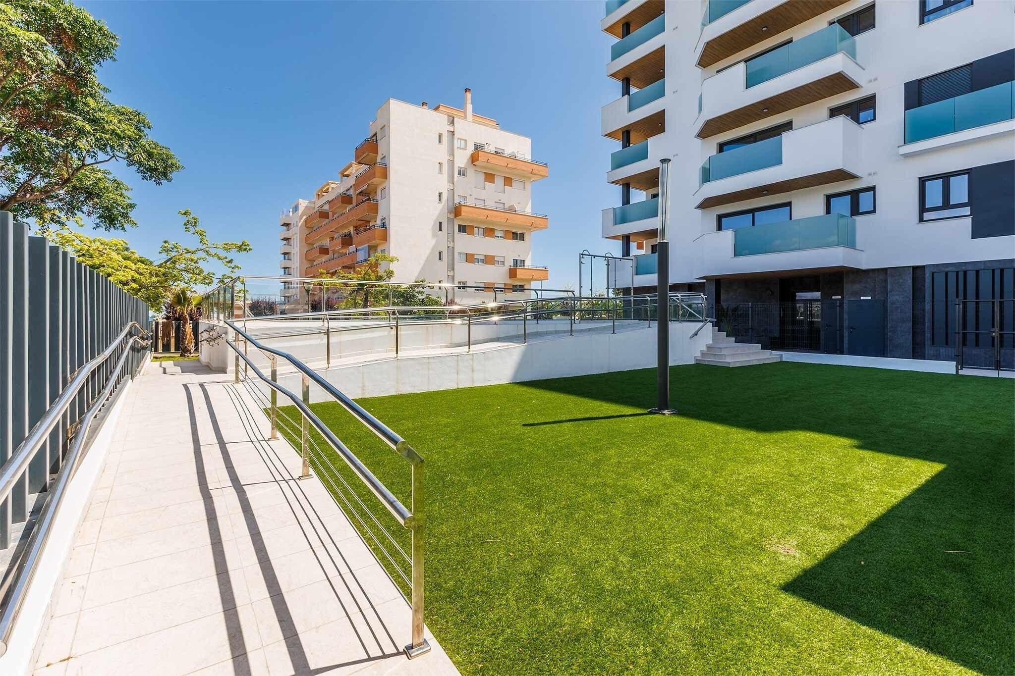 Un moderno complejo de apartamentos con un patio cubierto de césped, balcones y cielo despejado.
