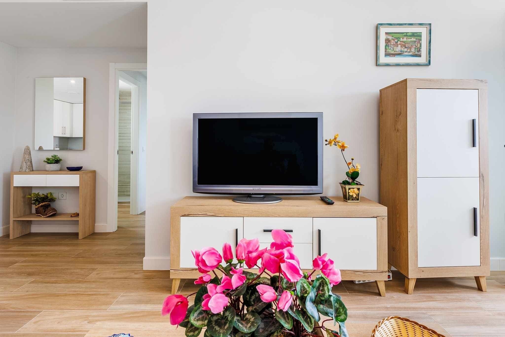 A modern living room with a flat-screen TV on a wooden cabinet, a white wardrobe, and a mirror on the wall.