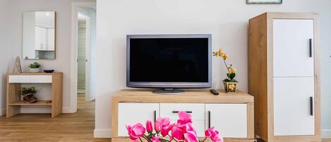 A modern living room with a flat-screen TV on a wooden cabinet, a white wardrobe, and a mirror on the wall.