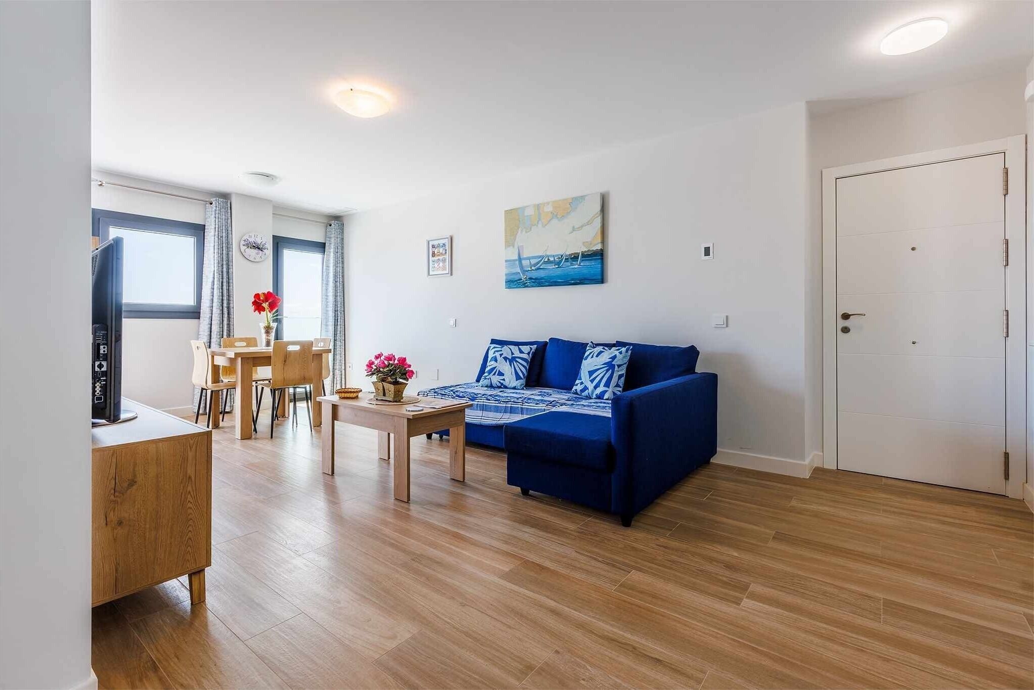 A modern living room with a blue sofa, wooden flooring, and a dining area with a table and chairs.