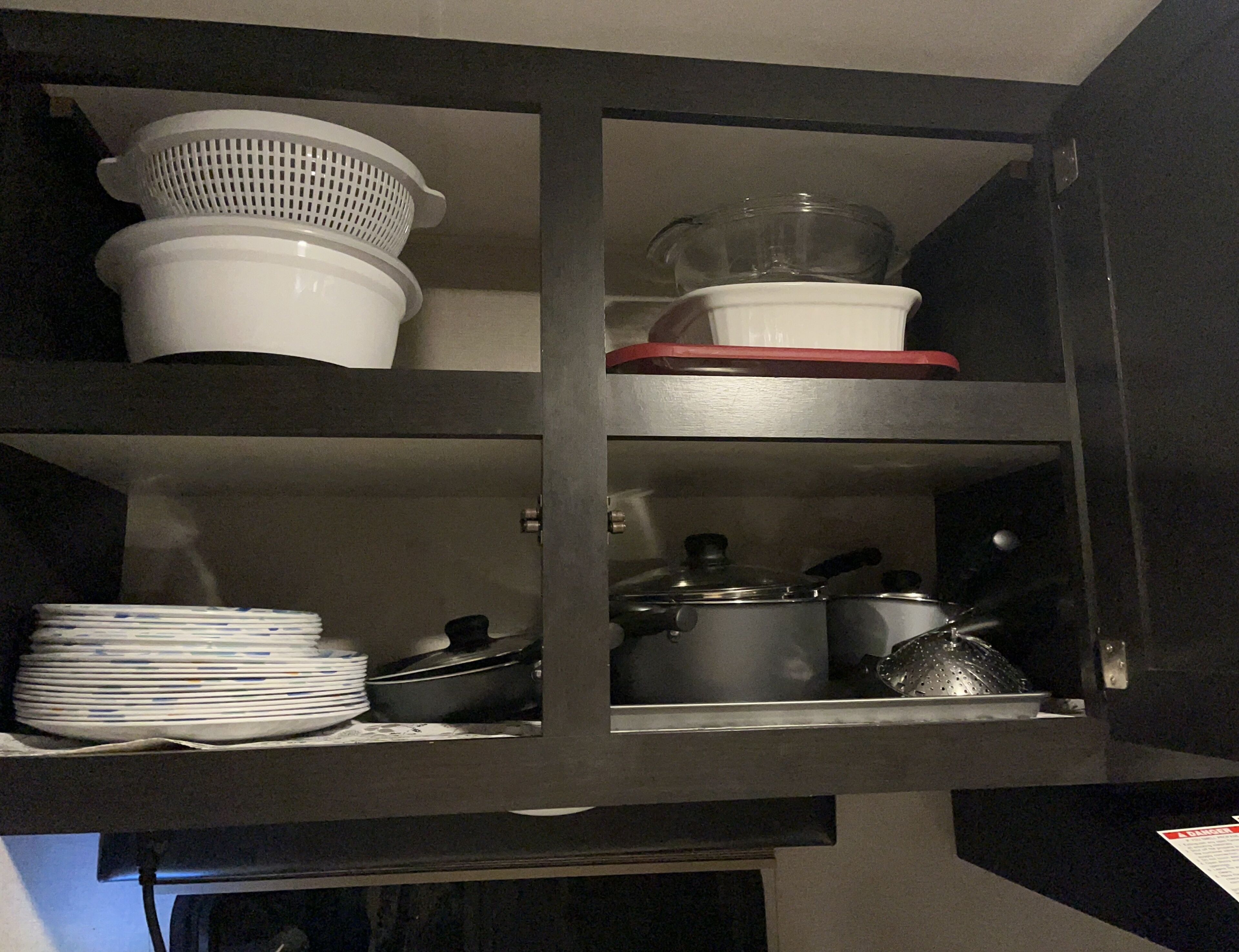 A kitchen cabinet with shelves holding various kitchen items including a colander, pots, and plates.