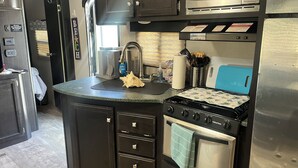 A compact kitchen with a stove, oven, microwave, and a sink. - ONSITE 2019 RV, Camping, South Haven, MI (South Haven)