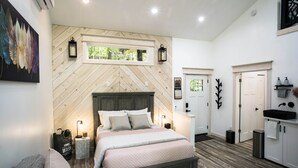A bedroom with a wooden herringbone wall, a bed with a headboard, bedside tables, a window, and a view of the outdoors. - Luxury Treehouse 20 miles from asheville.  (Saluda)