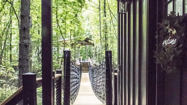 A wooden deck leading to a building with a 'Welcome' sign, surrounded by trees. - Luxury Treehouse 20 miles from asheville.  (Saluda)