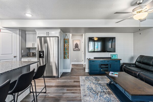 A modern kitchen with a central island, bar stools, a built-in refrigerator, and a dining area with a wooden table and chairs.