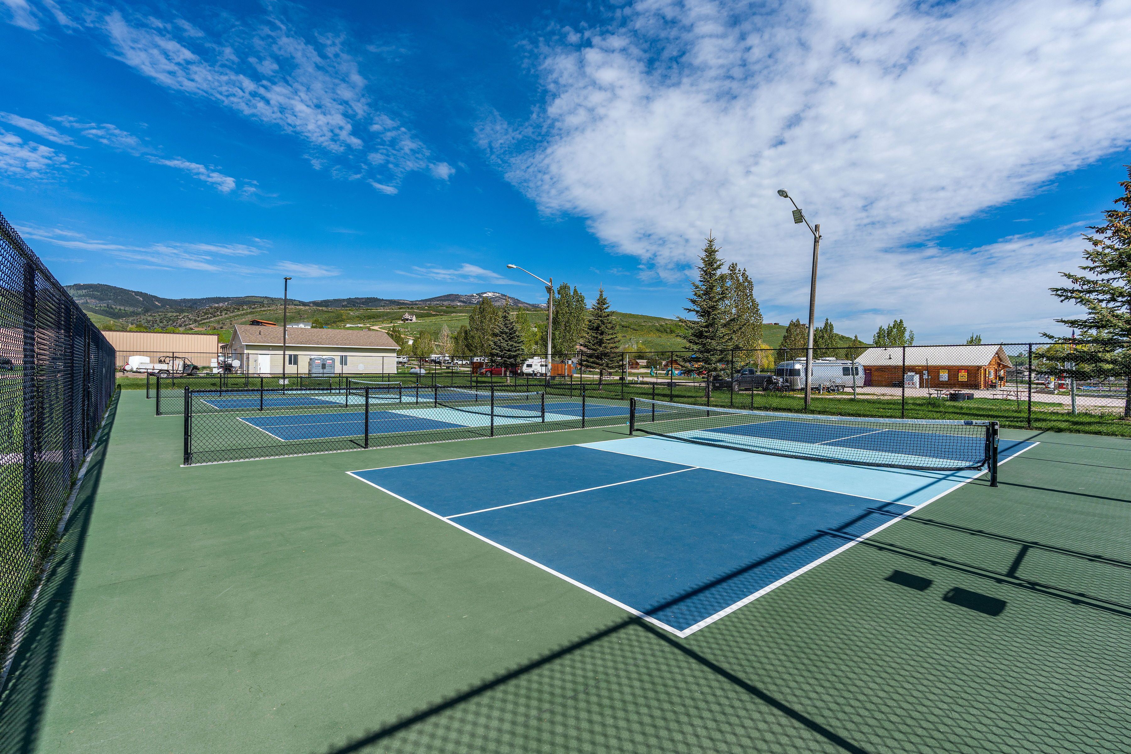 Ein Tennisplatz im Freien mit mehreren Spielfeldern, umzäunt, mit Gebäuden und Bergen im Hintergrund.