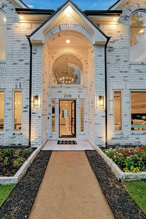 Une maison moderne avec une façade en briques, une grande entrée en arc de cercle et le numéro « 21318 » affiché au-dessus de la porte.