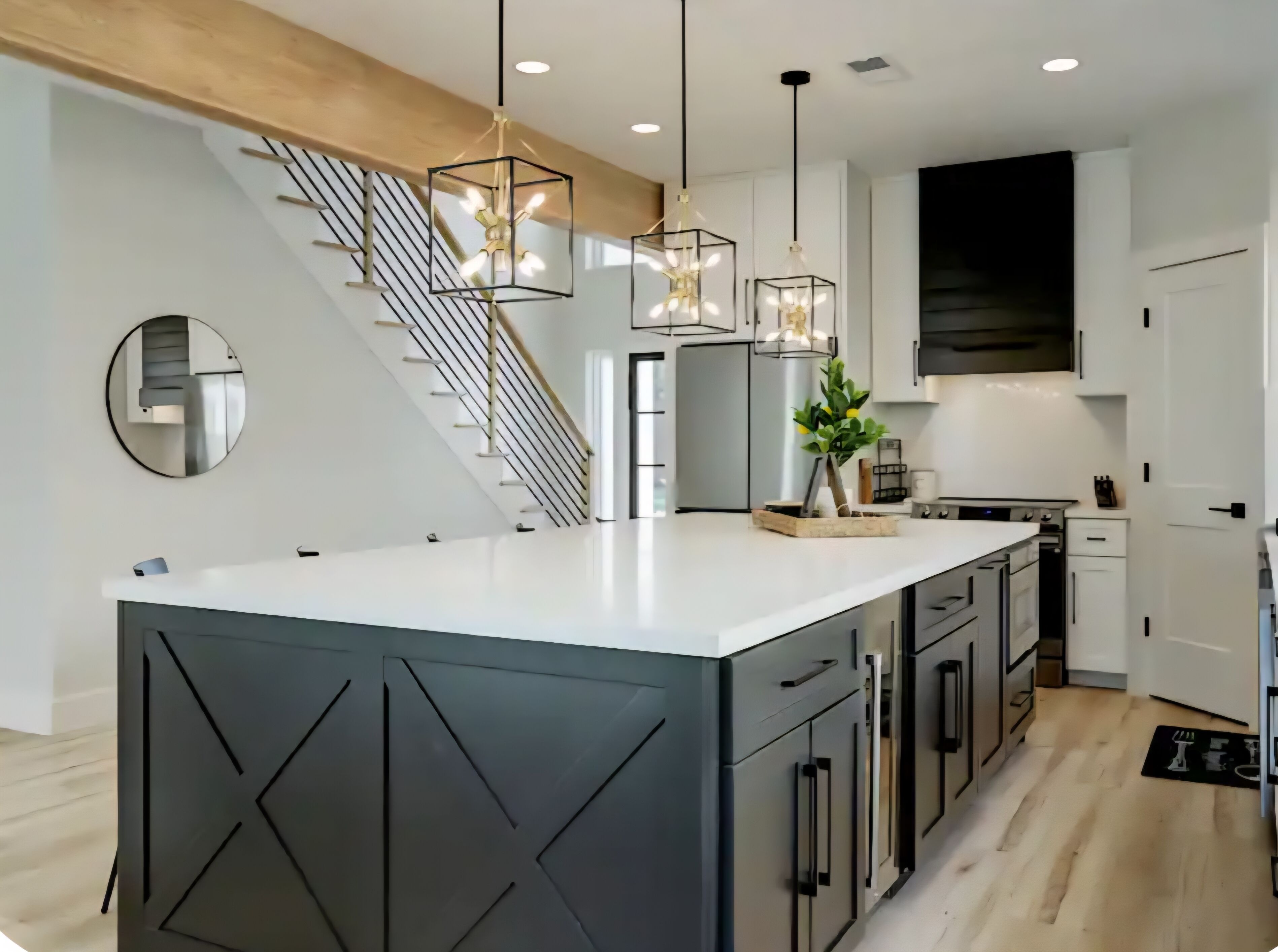 A modern kitchen with a central island, stainless steel appliances, and a staircase with a glass railing.