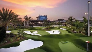 A golf course with sand bunkers, palm trees, and a building with a sign. - Modern Farmhouse • Chef Kitchen • GameRoom • 77" OLED • BBQ Grill  (Katy)