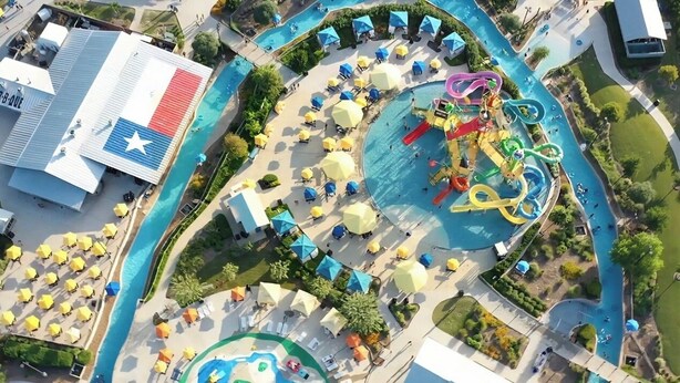 An aerial view of a water park with a swimming pool, water slides, and sun umbrellas. - Modern Farmhouse • Chef Kitchen • GameRoom • 77" OLED • BBQ Grill  (Katy)
