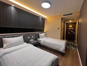 A hotel room with two beds, a bedside table with a lamp, a wall-mounted TV, and a door with a 'No Smoking' sign. - Hennessy Hotel (Hong Kong)