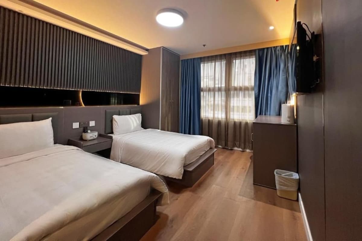A hotel room with two beds, a TV, a desk, and a window with curtains.
