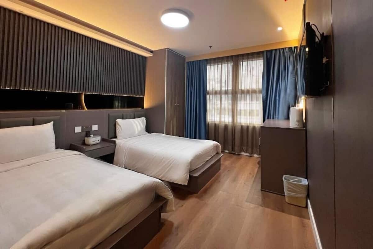 A hotel room with two beds, a TV, a desk, and a window with curtains.