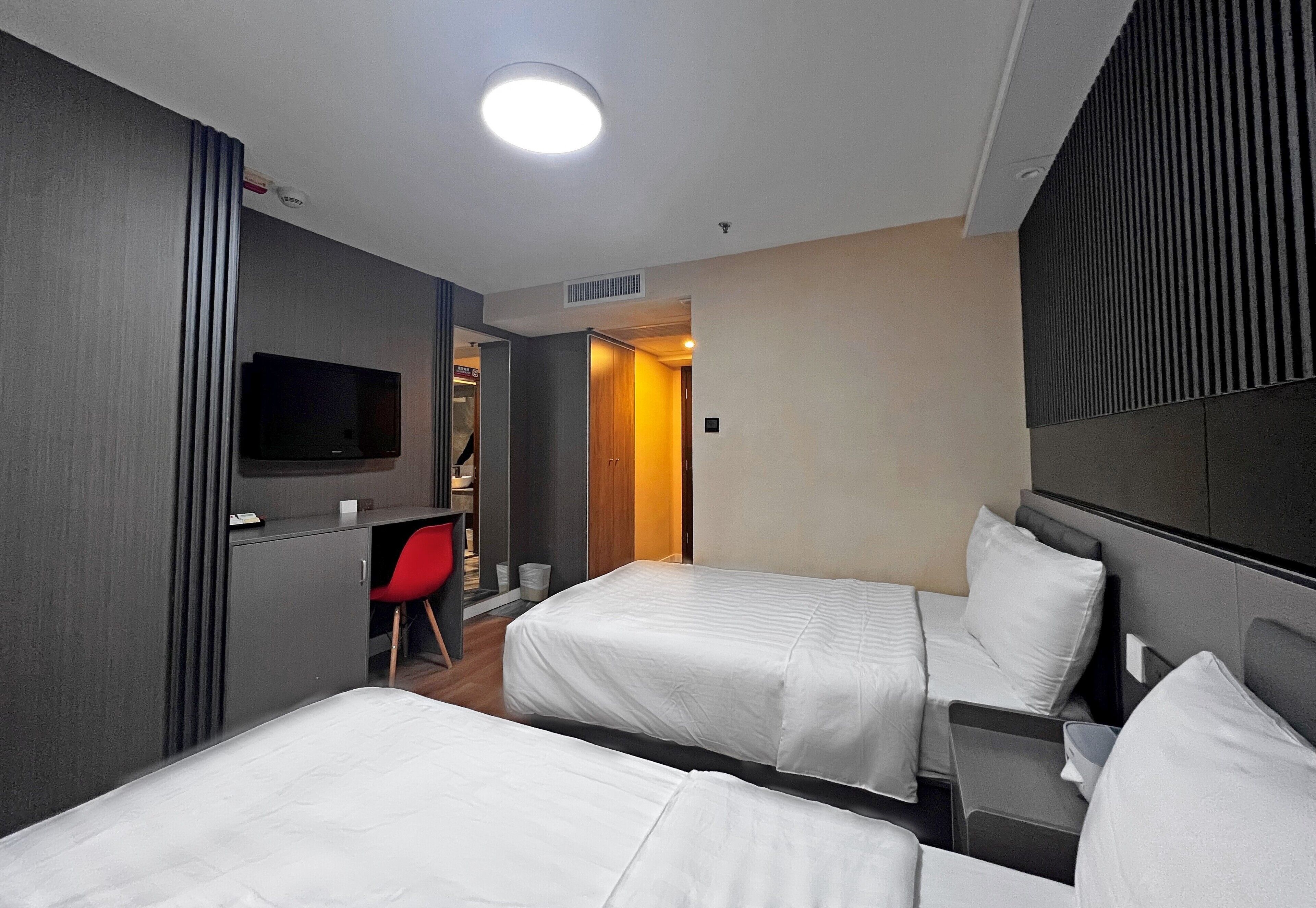 Habitación de hotel con dos camas, un televisor, un escritorio y una silla roja.