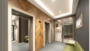 A modern hotel lobby with a herringbone wood panel wall, a green seating area, and a glass elevator. - Hennessy Hotel (Hong Kong)