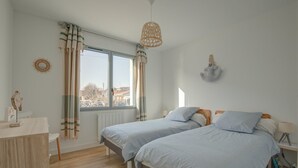 Un dormitorio con dos camas, una ventana con cortinas, una mesita de noche con lámpara y un adorno en la pared.