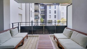 A balcony with two sofas and a wooden floor, overlooking a residential area with multiple buildings.