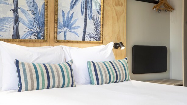 Camera d'albergo con un letto, cuscini a righe, una testiera con un dipinto di palme e un pannello testiera nero.