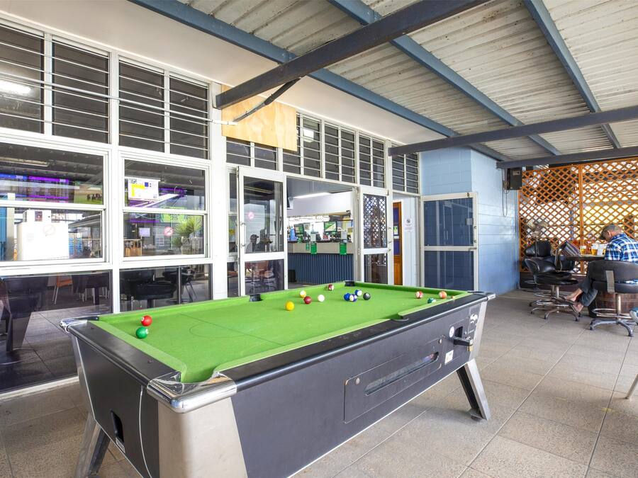 A pool table in a room with large windows and a covered area with chairs and tables.