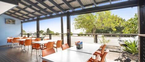 An outdoor patio with tables and chairs, a covered area, and a view of the street and trees.