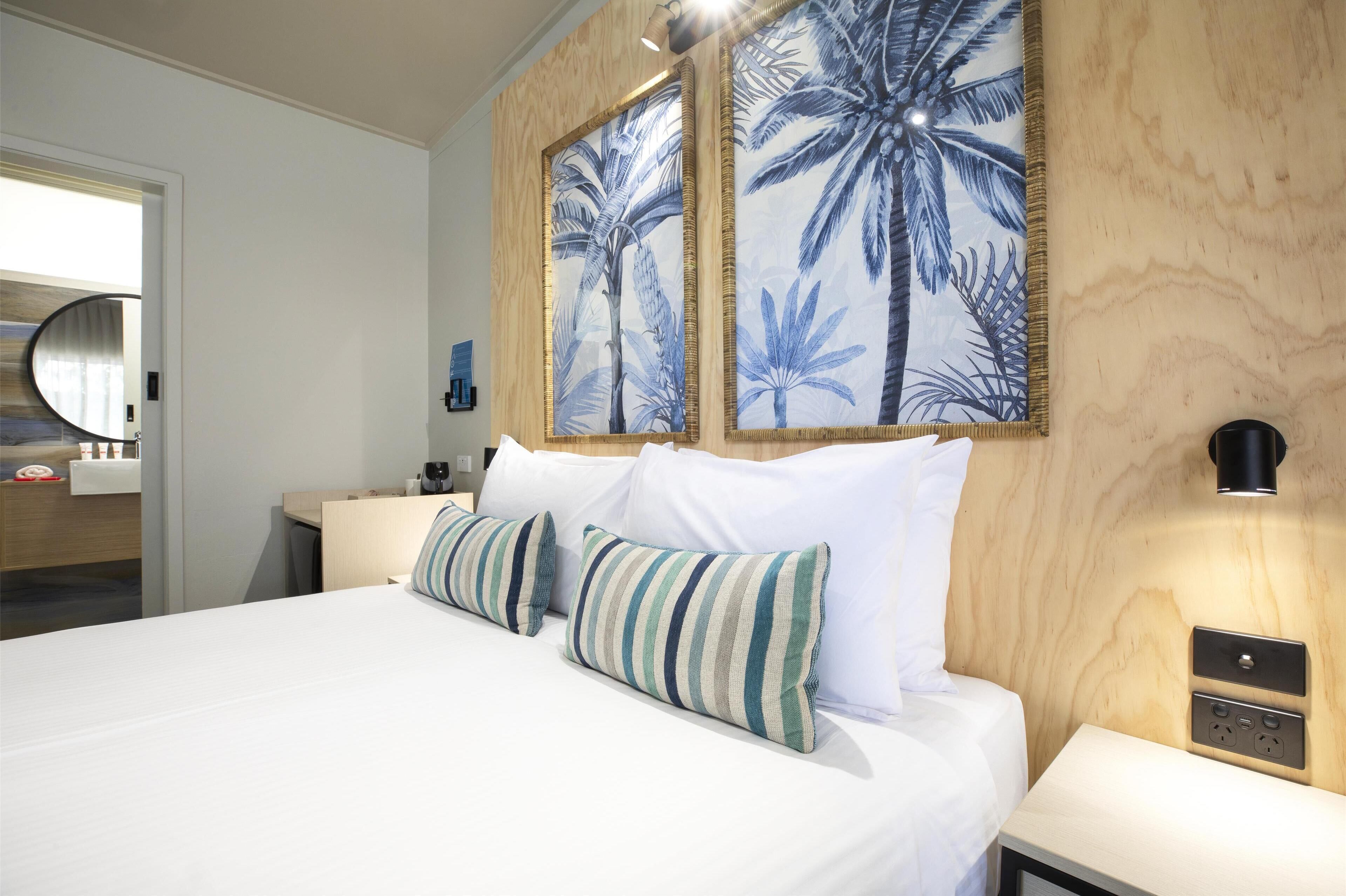 Ein Hotelzimmer mit einem großen Bett, zwei Wandleuchten, einer Holzwand und einem Spiegel.