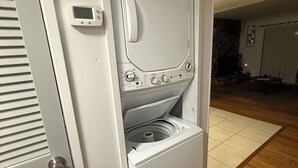 Ein Waschraum mit einer Waschmaschine und einem Trockner mit Frontlader, einem Thermostat und einem Kamin aus Stein im Hintergrund.