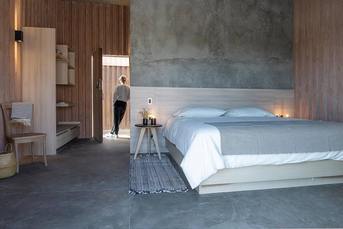 A modern bedroom with a large bed, a wooden wardrobe, and a concrete ceiling.