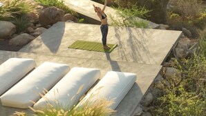 A person performing yoga on a mat in a natural outdoor setting with rocks and cacti. - Casa Santos (Todos Santos)