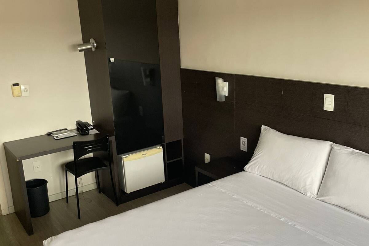Habitación de hotel con una cama grande, un escritorio, una silla, un cesto de basura pequeño y un minibar.