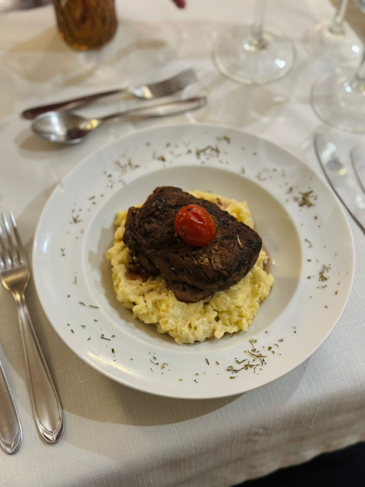 A plate with a meat dish and mashed potatoes, accompanied by a fork and spoon on a table.