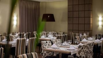 Un restaurante con mesas dispuestas para comer, sillas y un gran ventanal con cortinas.