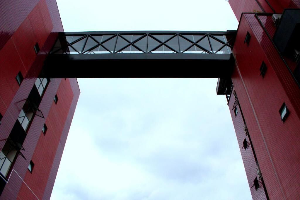 A tall red building with a black bridge-like structure connecting two sections.