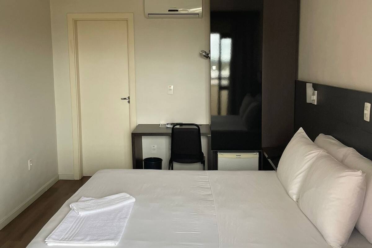 Una habitación de hotel con una cama, un escritorio, una silla y un equipo de aire acondicionado.
