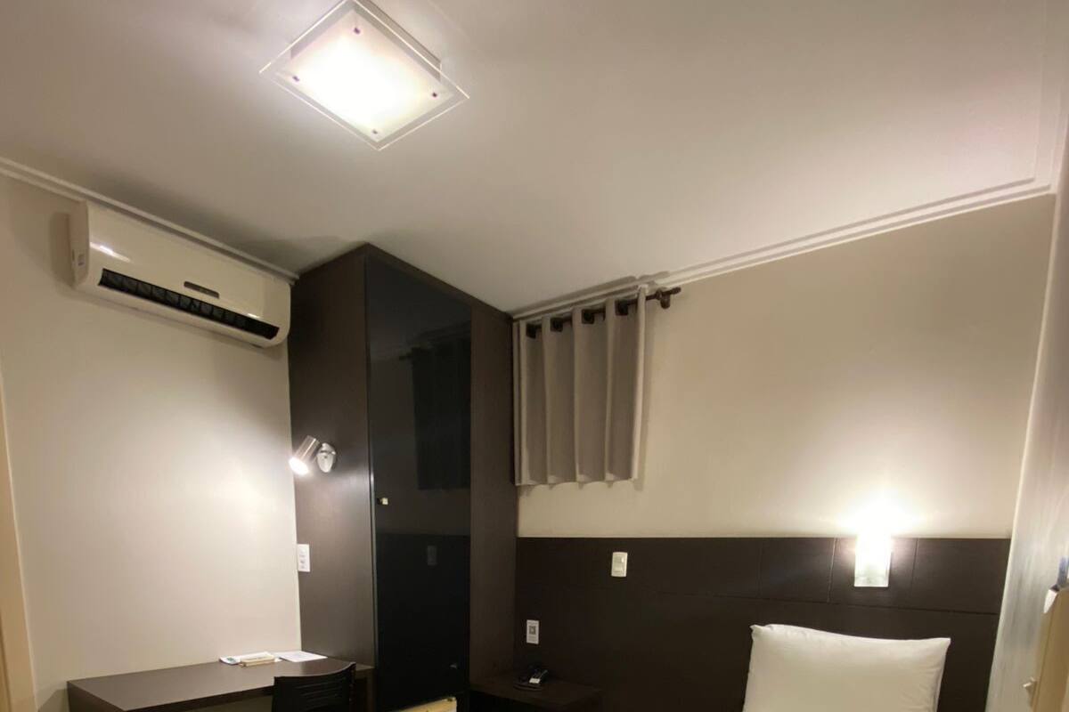 Habitación de hotel con cama, escritorio, silla, mesita de noche y equipo de aire acondicionado.