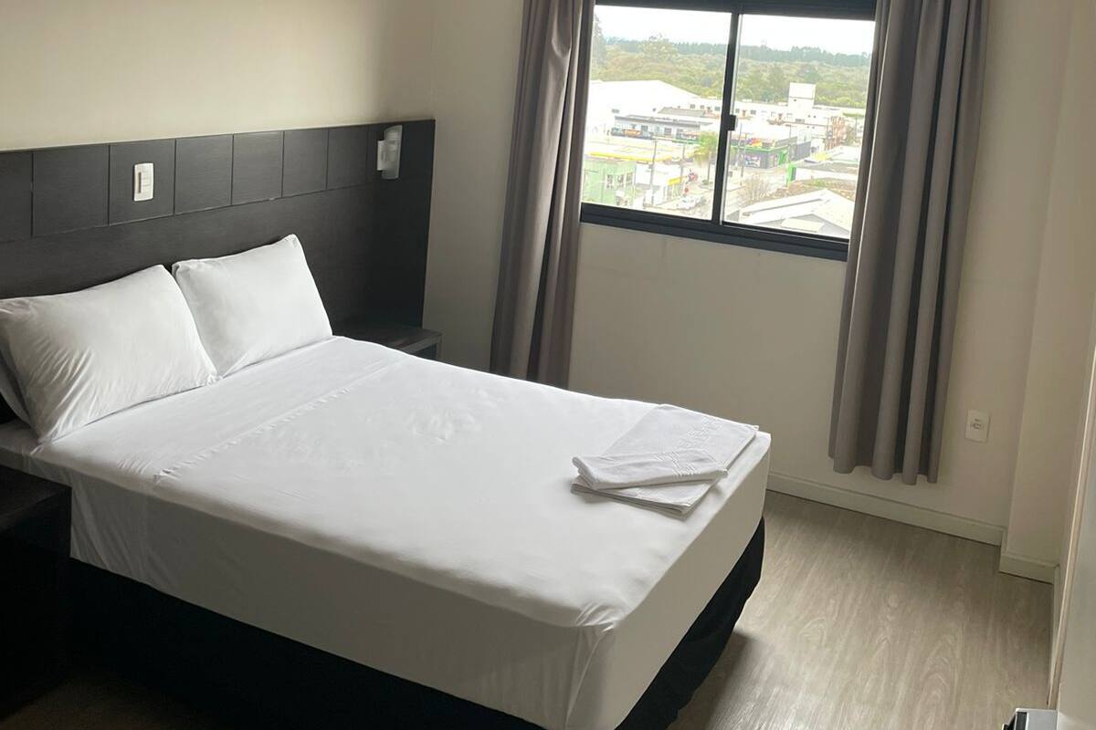 Una habitación de hotel con una cama, una mesita de noche, una ventana con cortinas y vistas al exterior.