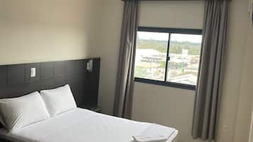 Una habitación de hotel con una cama, una mesita de noche, una ventana con cortinas y vistas al exterior.
