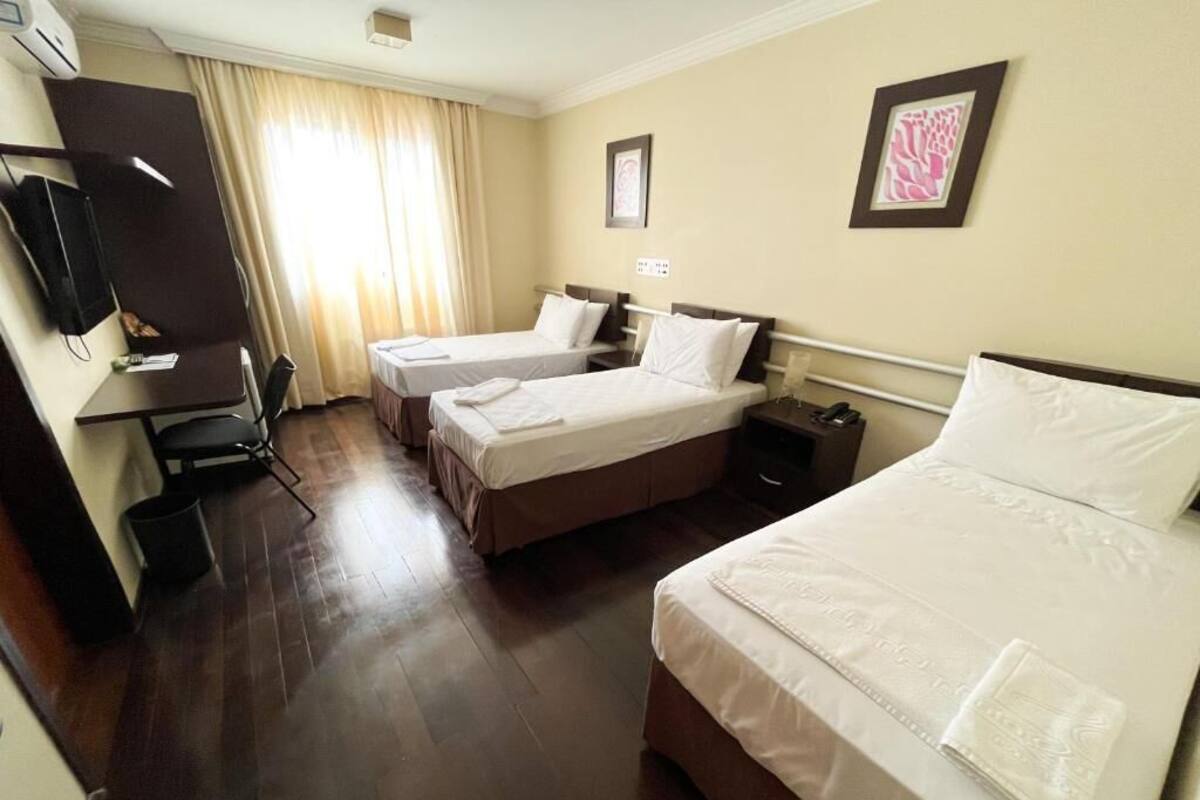 Una habitación de hotel con dos camas individuales, un escritorio con silla, televisión y ventana con cortinas.