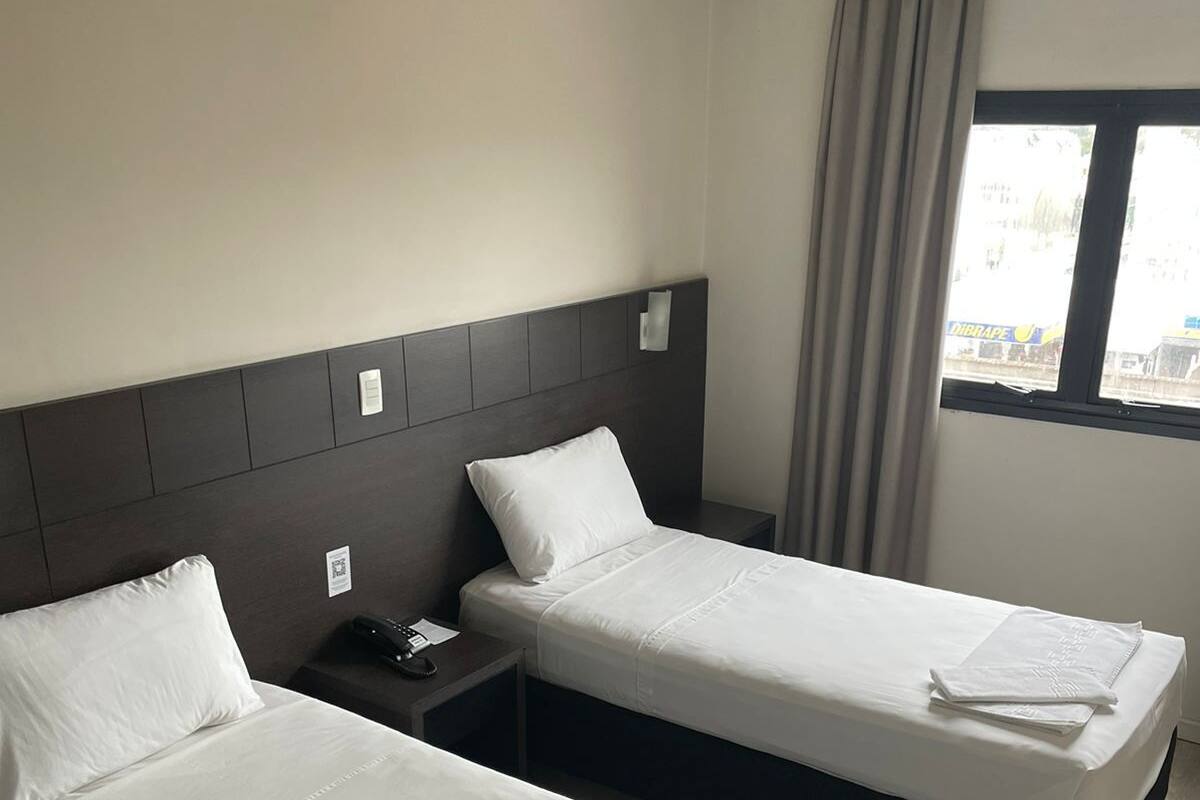 Habitación de hotel con dos camas, una mesita de noche y una ventana con cortinas.