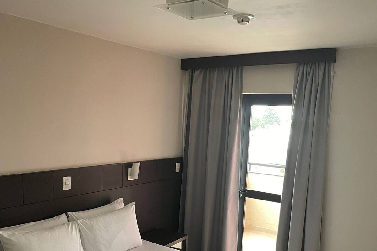 Habitación de hotel con una cama grande, cabecera, lámpara de techo y ventana con cortinas.