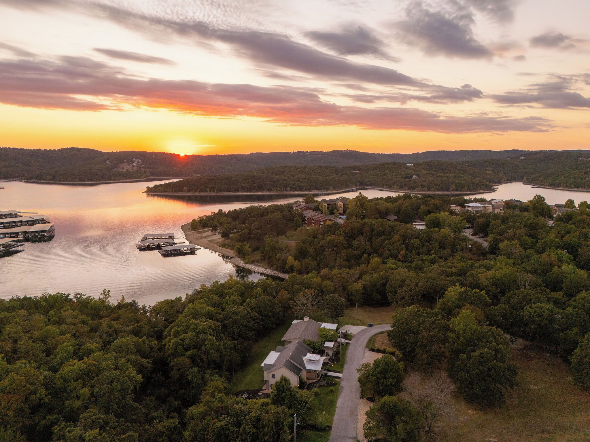 Une propriété au bord du lac, dotée d’un quai, entourée d’une forêt dense, avec un coucher de soleil en arrière-plan.