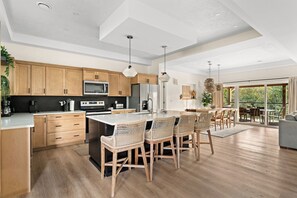 A modern kitchen with wooden cabinets, a central island with bar stools, and a dining area with a large table and chairs.