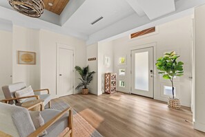 A spacious living area with a wooden floor, a seating arrangement with chairs and a sofa, a potted plant, and a door with a window.