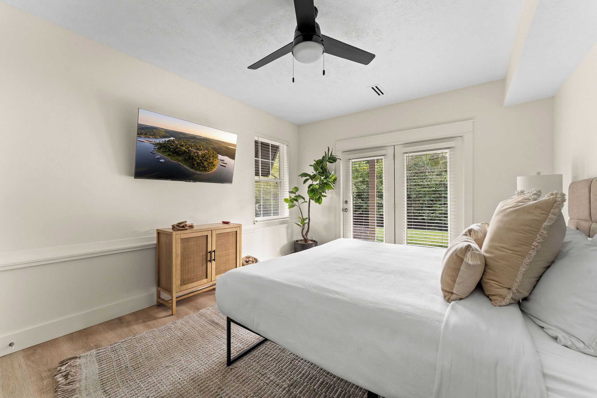 Un dormitorio con cama, televisor montado en la pared, ventilador de techo y ventana con persianas.