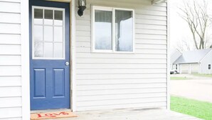 Una casa con puerta azul, un pequeño porche y un felpudo rojo con la palabra 'Love'.