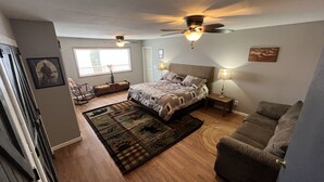 Een slaapkamer met een bed, twee plafondventilatoren, een nachtkastje, een lamp, een bank, een raam en een vloerkleed.