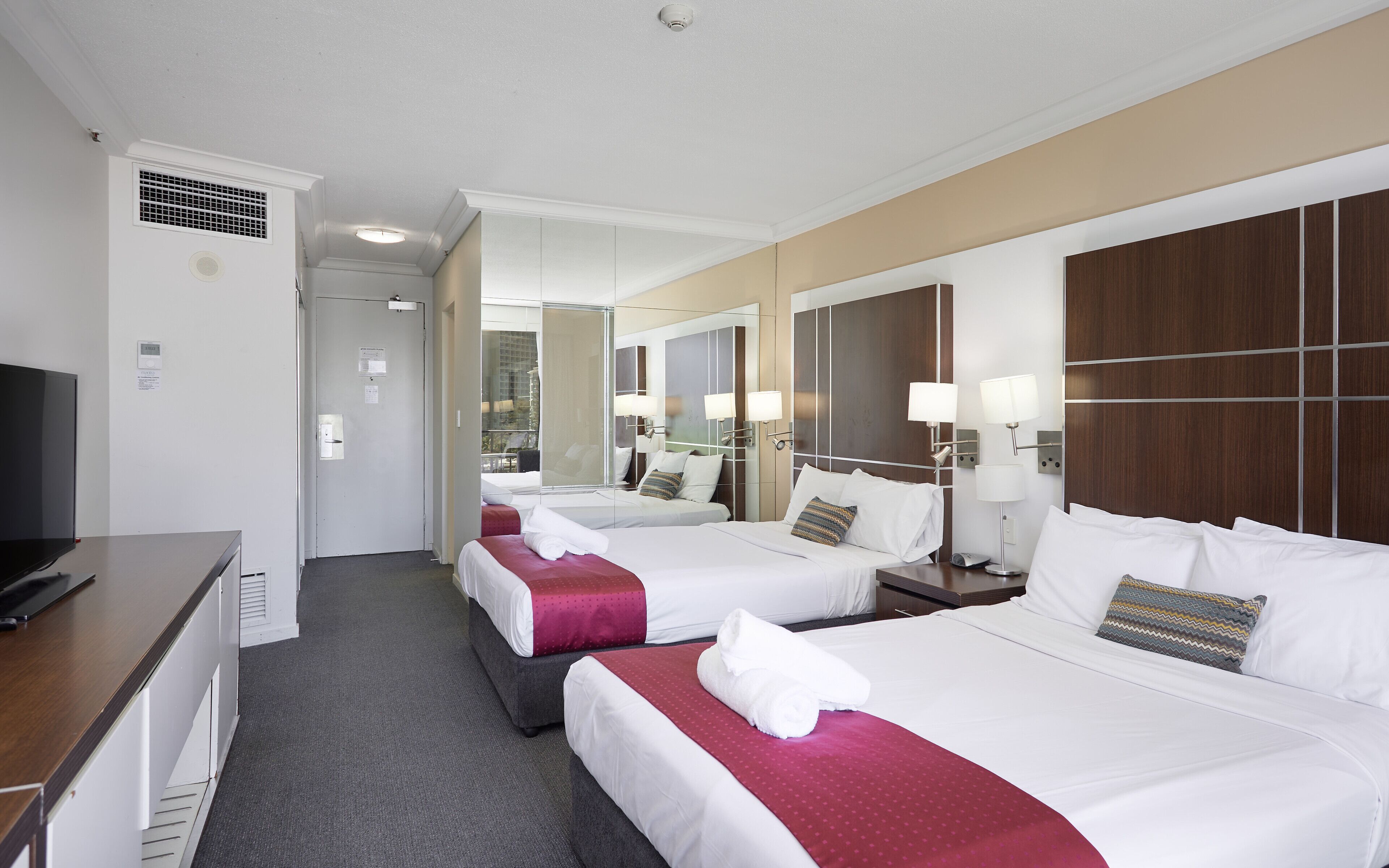 Habitación de hotel con dos camas, televisión, escritorio y espejo.